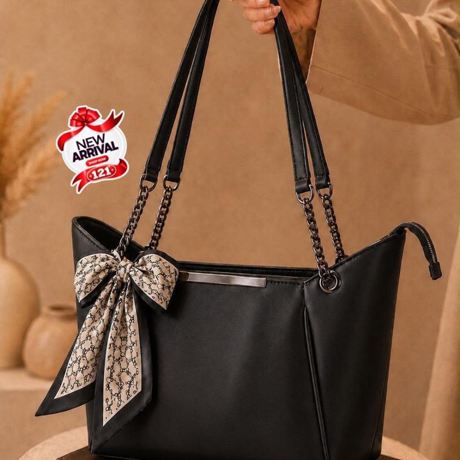 A black leather tote bag with a large beige patterned scarf bow on the front
