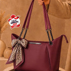 A burgundy tote handbag with a matching fabric bow and patterned scarf accent