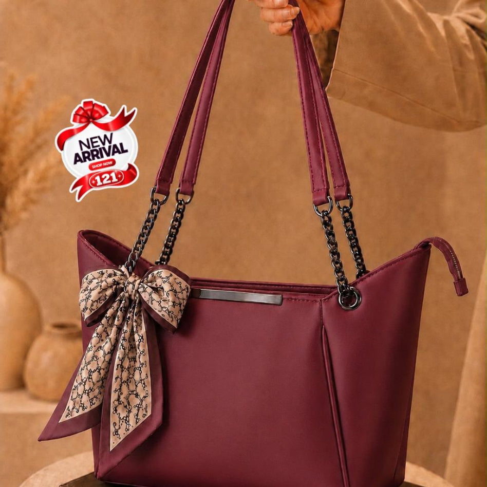 A burgundy tote handbag with a matching fabric bow and patterned scarf accent