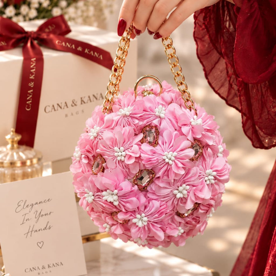 A pink floral ball purse with a gold chain strap and rhinestone embellishments